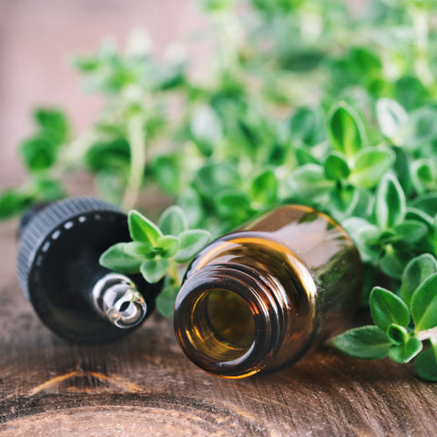 On a wooden table, Thyme surrounds a tipped over amber-colored bottle