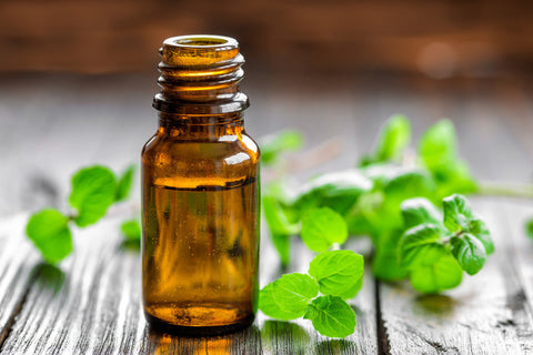 An oil-filled amber-colored bottle sits on a wooden table with peppermint leaves around it