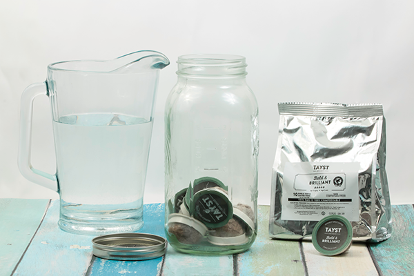 bag of tayst coffee beans next to jug of water and a mason jar filled with tayst coffee pods