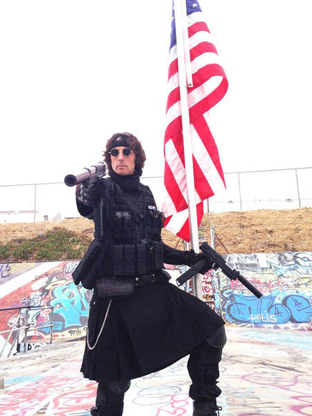 paintball player wearing a kilt and standing in front of an American flag