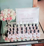 alt="Baby shower nail varnish favours. Bottles with personalised labels stood in front of thank you plaque and flowers"