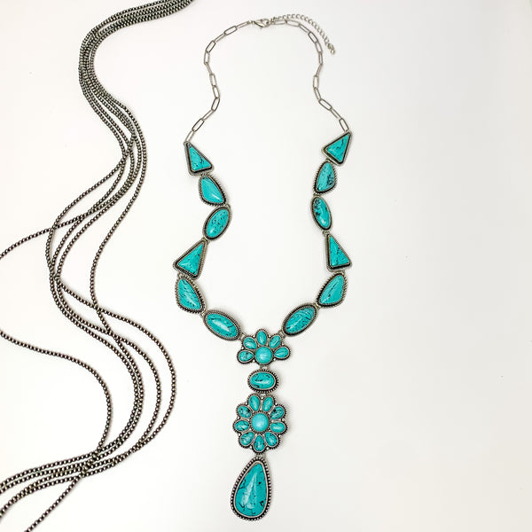 Multi stoned long necklace in turquoise with a dangling flower cluster. Pictured on a white background with Navajo pearl stands.