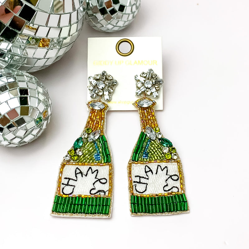 Festive Jeweled and Beaded Champagne Bottle Earrings. Pictured on a white background with disco balls in the top left.