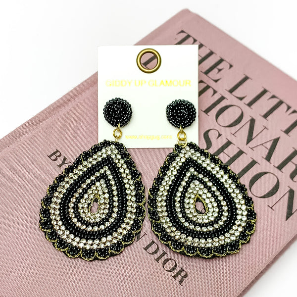 Sound Wave Beaded Drop Earrings with Clear Crystals in Black. Pictured on a white background with a book behind the earrings.