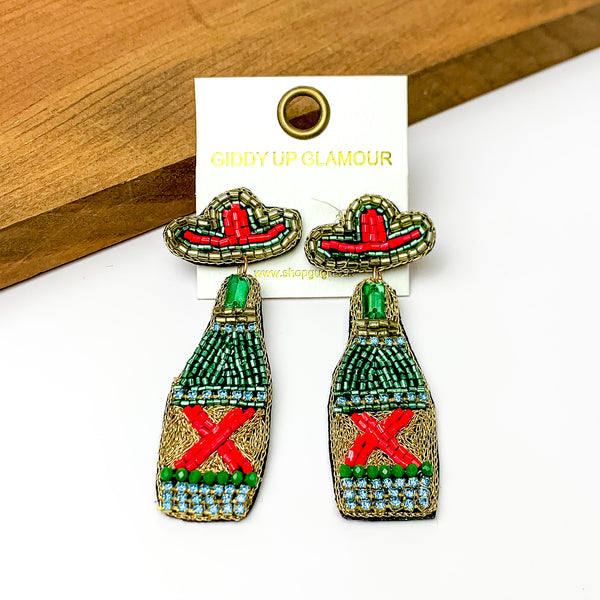 Beaded Green Beer Bottle Earrings with Sombrero Studs. Pictured on a white background with a wood piece at the top.