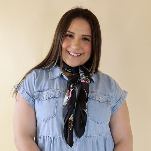 Brunette model wearing a blue dress with Multicolored print scarf tied around her neck. Model is pictured in front of a beige background.