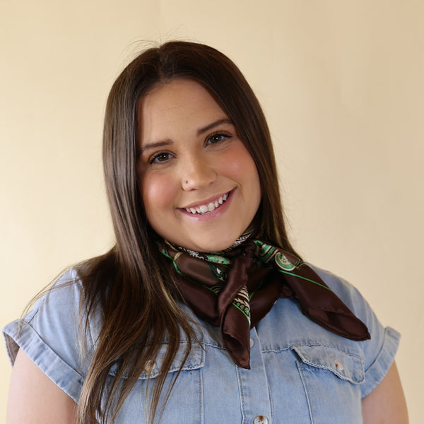 Brunette model wearing a blue dress with Green and Brown scarf tied around her neck. Model is pictured in front of a beige background.