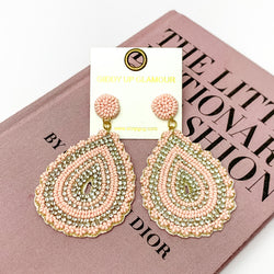 Sound Wave Beaded Drop Earrings with Clear Crystals in Light Pink. Pictured on a white background with a book behind the earrings.