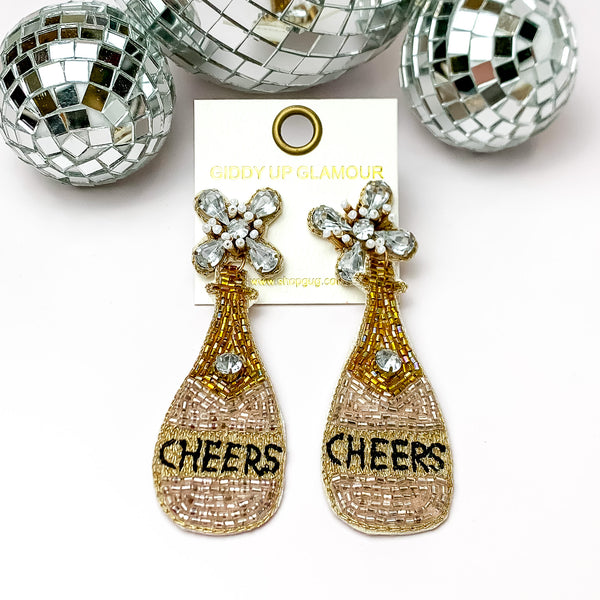 Cheers to These Beaded and Jeweled Champagne Bottle Earrings. Pictured on a white background with disco balls at the top for decor.