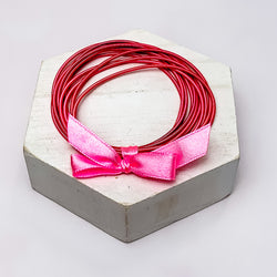 Guitar String Bracelets with Bow in Dark Pink. Pictured on a white background sitting on top of a white block.