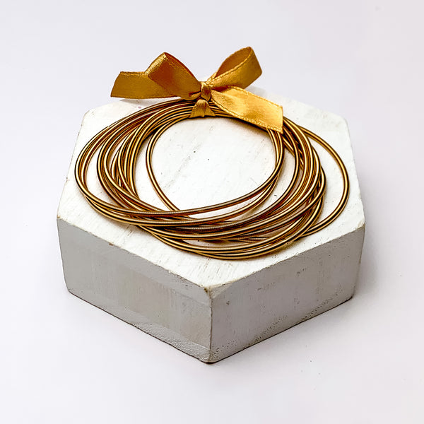 Guitar String Bracelets with Bow in Gold Tone. Pictured on a white background sitting on top of a white block.