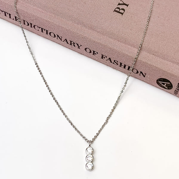 Triple Clear Crystals Silver Tone Necklace. Pictured on a white background with the necklace laying on a book.