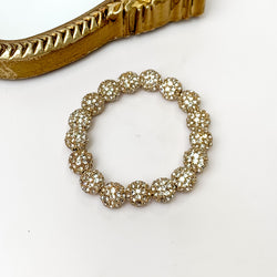 Clear crystal beaded bracelet with a gold setting is pictured on a white background with a gold mirror in the top left corner. 