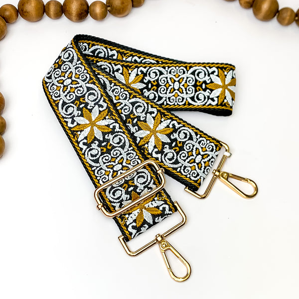 Black canvas purse strap with white and gold embroidered design. This purse strap includes gold accents. This purse strap is pictured on a white background with wood beads at the top.