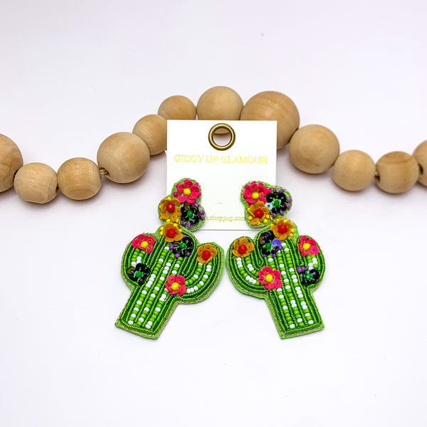 Beaded Cactus Post Earrings With Multicolor Flowers in Light Green. Pictured on a white background with the earrings laying against wood beads.