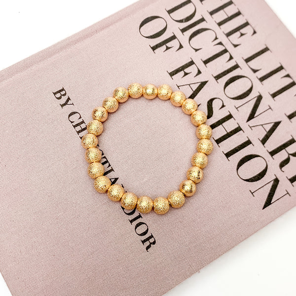 Gold Tone Basic Beaded Bracelet. Pictured laying on a book. The book is on a white background.