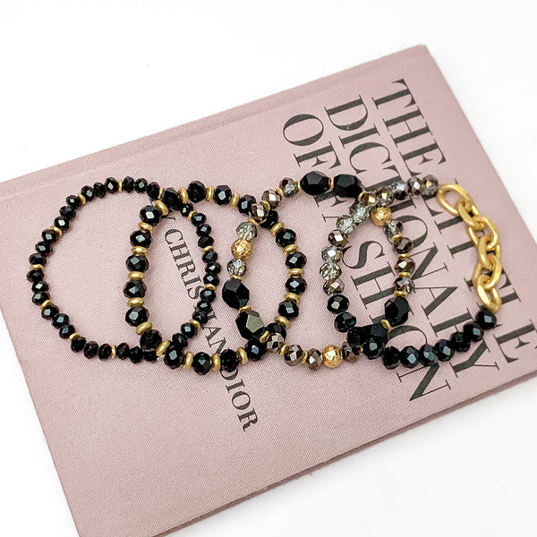 Set of Four | Glorious Gold Crystal Beaded Bracelet Set in Black. Pictured laying on a closed book. The book is on a white background.