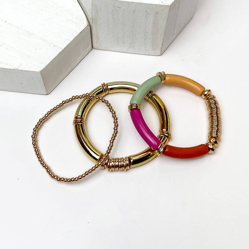 Set of Three | Bahama Nights Gold Tone Tube Bracelet Set in Multicolor. Pictured on a white background with white platforms above the bracelets. 