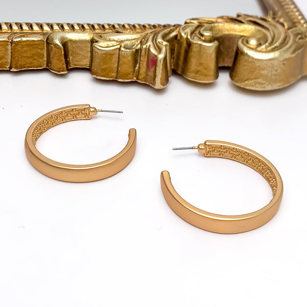 Gold Tone Large Hoop Earrings With a Textured Inside. Pictured on a white background with a gold frame above the picture.