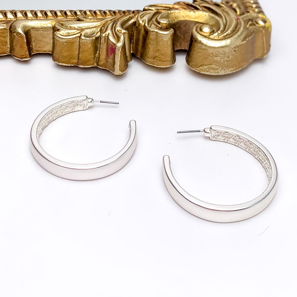 Silver Tone Large Hoop Earrings With a Textured Inside. Pictured on a white background with a gold frame above the earrings.