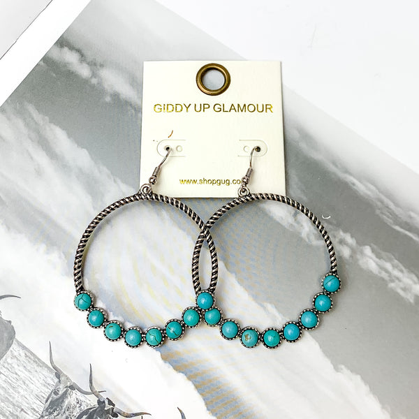 Forever Twisted Hoop Earrings with Stones in Turquoise. Pictured on an open book with a western scene behind the earrings.