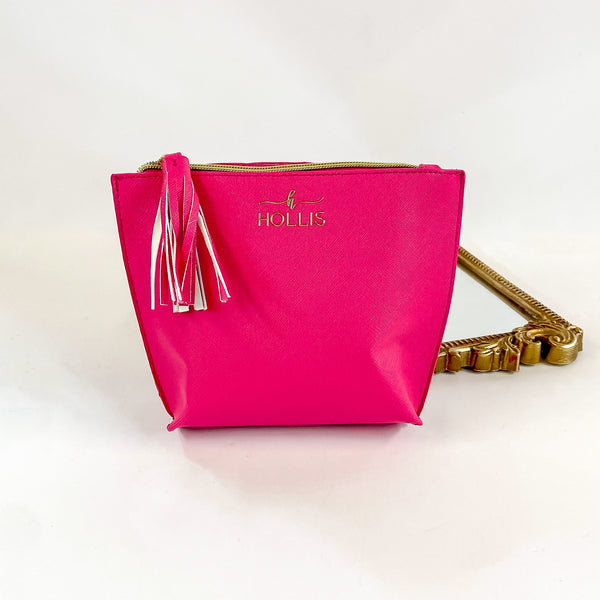 Smaller sized hot pink zip up bag with tassel charm Pictured on a white background with a mirror behind. 