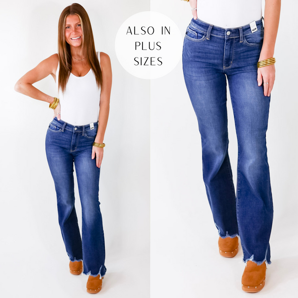 Model is wearing a pair of dark wash bootcut jeans with a raw hem. Model has these jeans paired with a white tank top, gold jewelry. and tan slip on wedges.