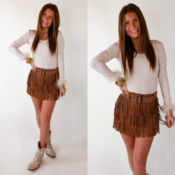 Model is wearing a cream colored long sleeve bodysuit featuring feathers on the end of the sleeves