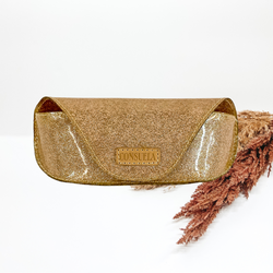 Gold glitter sunglasses case pictured on a white background that has tan and brown pompous grass on one side.