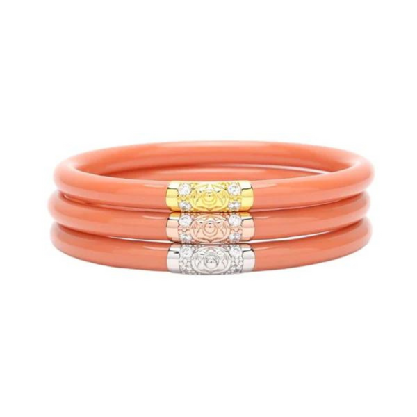 Three coral pink plastic, tube bracelet with one bracelet with a gold segment, one with a rose gold segment, and the other with a silver segment. These bracelets are pictured on top of each other on a white background. 