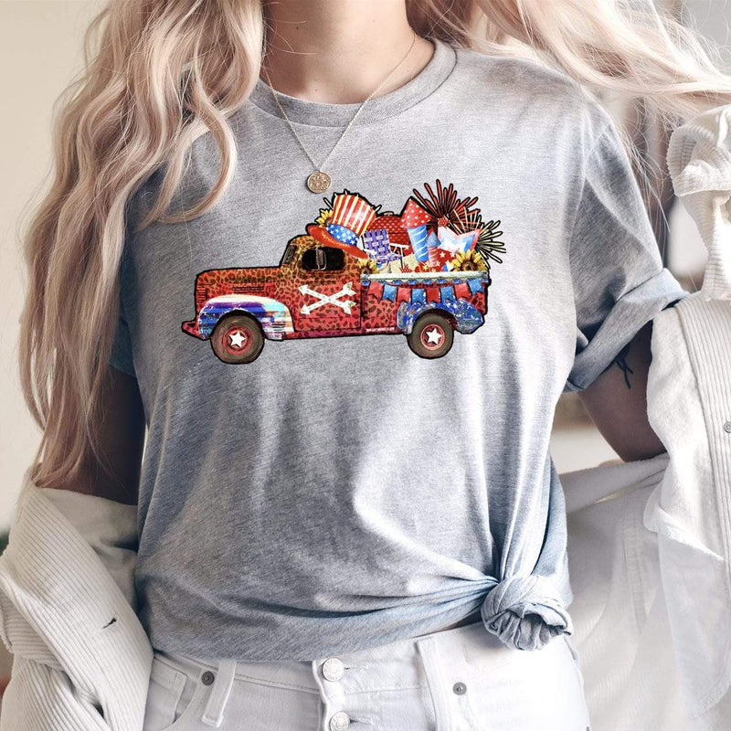 A heather gray short sleeve shirt with a graphic of a red, white, brown, and blue truck carrying fourth of July decorations and fireworks. 