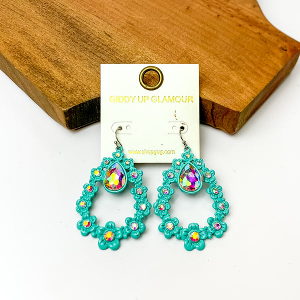 Turquoise open drop earrings with AB crystals and connecting flowers. Pictured on a white background with a wood piece at the top.