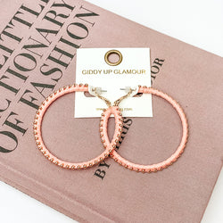  Pictured are circle light pink hoop earrings with gold beads around it. They are pictured with a pink fashion journal on a white background.