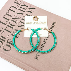 Pictured are circle beaded hoop earrings with gold spacers in green. They are pictured with a pink fashion journal on a white background