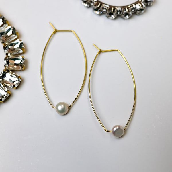 A pair of gold-tone cat eye hoop earrings with a pearl pendant at the bottom of each. Pictured on a white background with crystal necklaces.