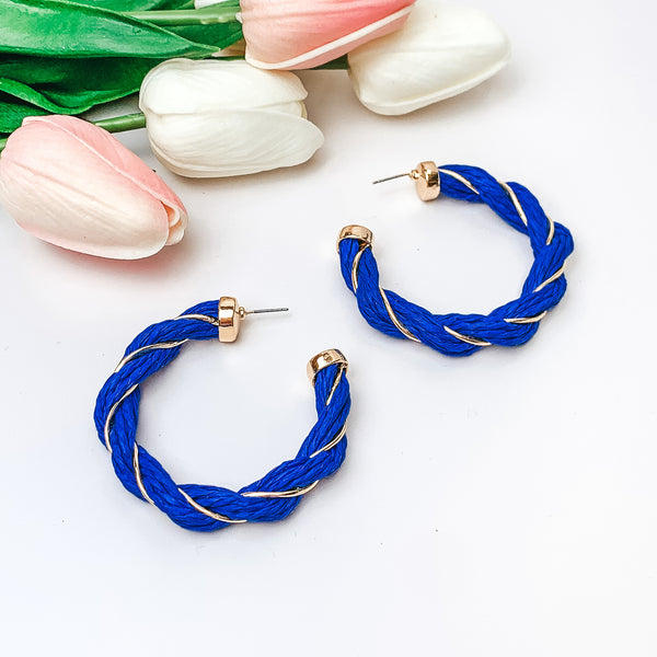 Pictured are blue raffia twisted hoop earrings with gold detailing.  They are pictured with pink and white tulips on a white background.