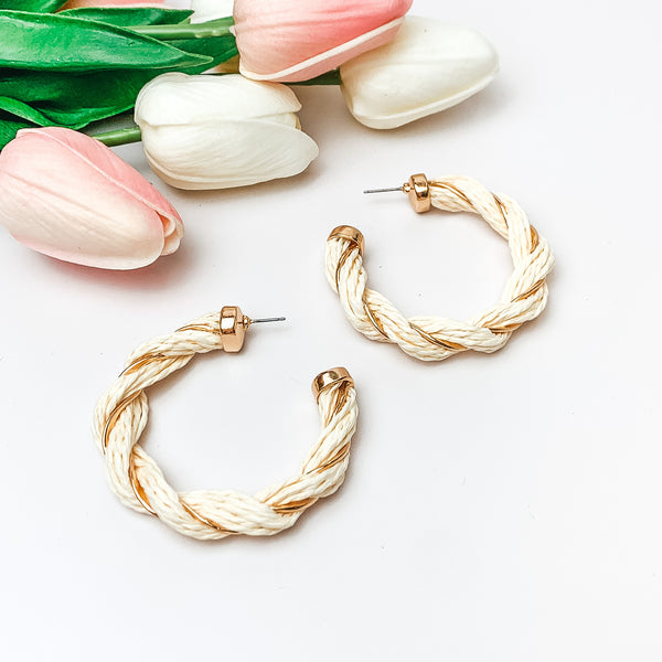 Pictured are ivory raffia twisted hoop earrings with gold detailing.  They are pictured with pink and white tulips on a white background.