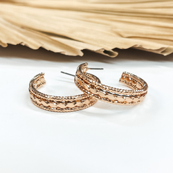 Open ended hoop earrings in gold with  different rope textures. These earrings are  pictured on a white background with a brown, dried up palm leaf in the back as decor.