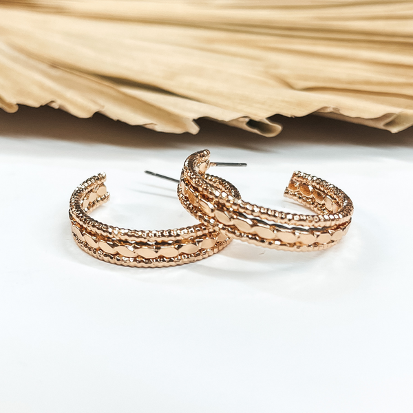 Open ended hoop earrings in gold with  different rope textures. These earrings are  pictured on a white background with a brown, dried up palm leaf in the back as decor.
