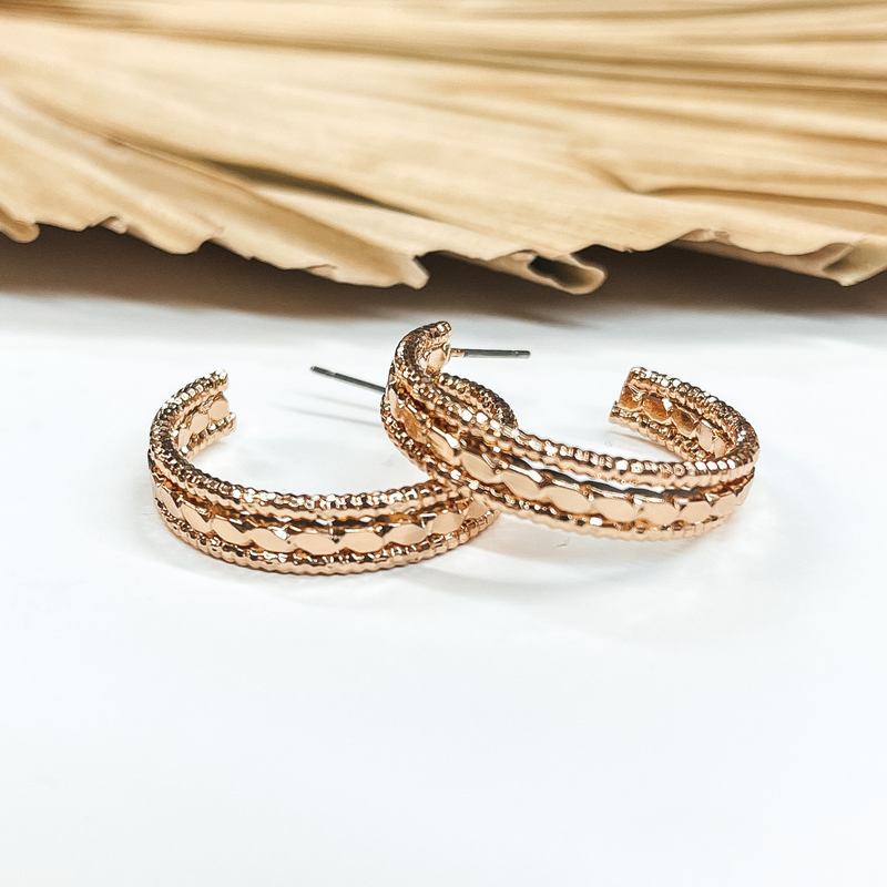 Open ended hoop earrings in gold with  different rope textures. These earrings are  pictured on a white background with a brown, dried up palm leaf in the back as decor.