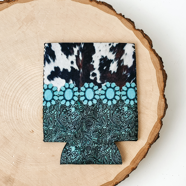 This Turqoise and Cowhide print kooozie is pictured on a peice of wood, with a white background.