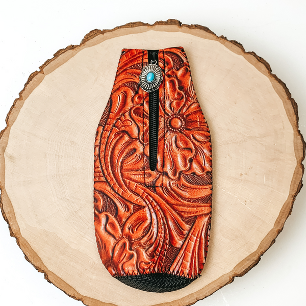 This Leather Tooled Print Zip Up kooozie With a Concho Charm is pictured on a peice of wood, with a white background.  