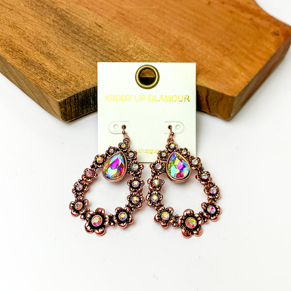 Copper tone open drop earrings with ab crystals and connecting flowers. Pictured on a white background with a wood piece at the top.