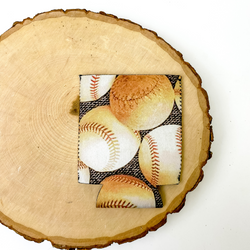 Baseball print koozie with dark grey background. This koozie is pictured on a piece of wood on a white background.