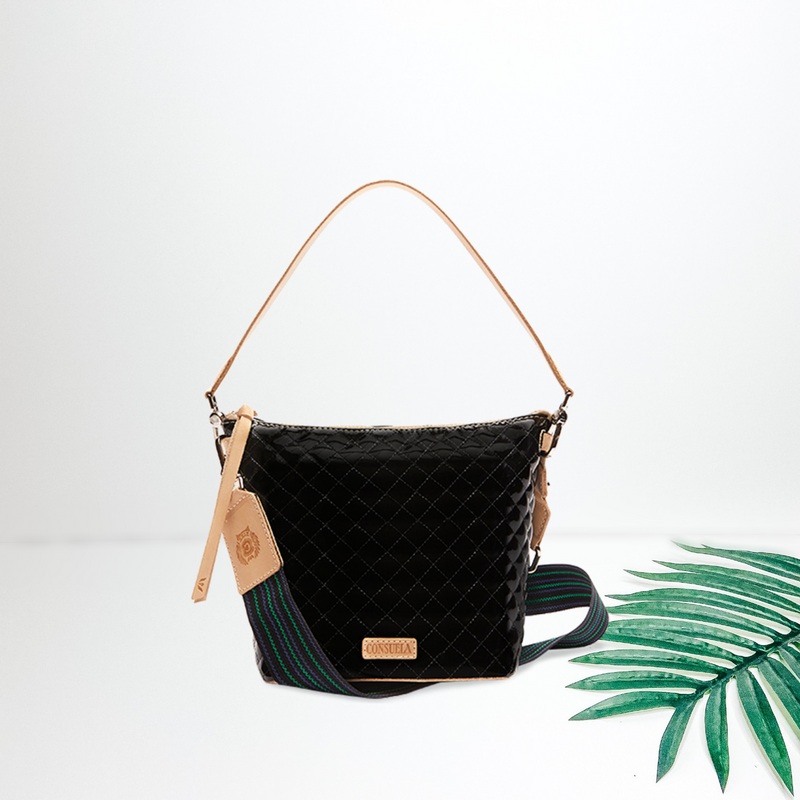 Pictured is a medium sized wedge bag with a handle and tassel on the left side, in a black quilted  pattern. On the right of the purse is a psalm leaf. Background is solid white.