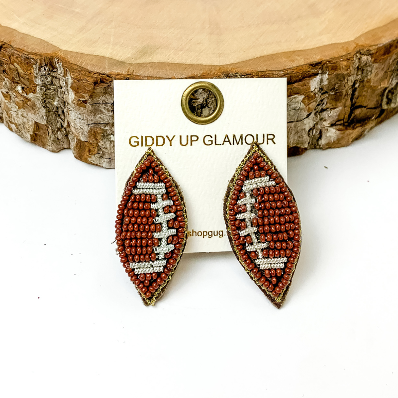Pictured are brown beaded stud football earrings. They are propped up on a circle piece of wood on a white background.