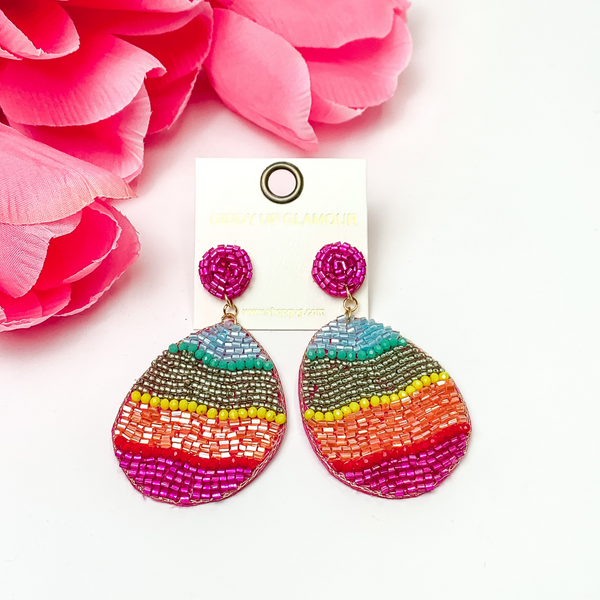 Beaded multi colored Easter egg. These earrings are pictured on a white background with red-coral flowers at the top left corner.