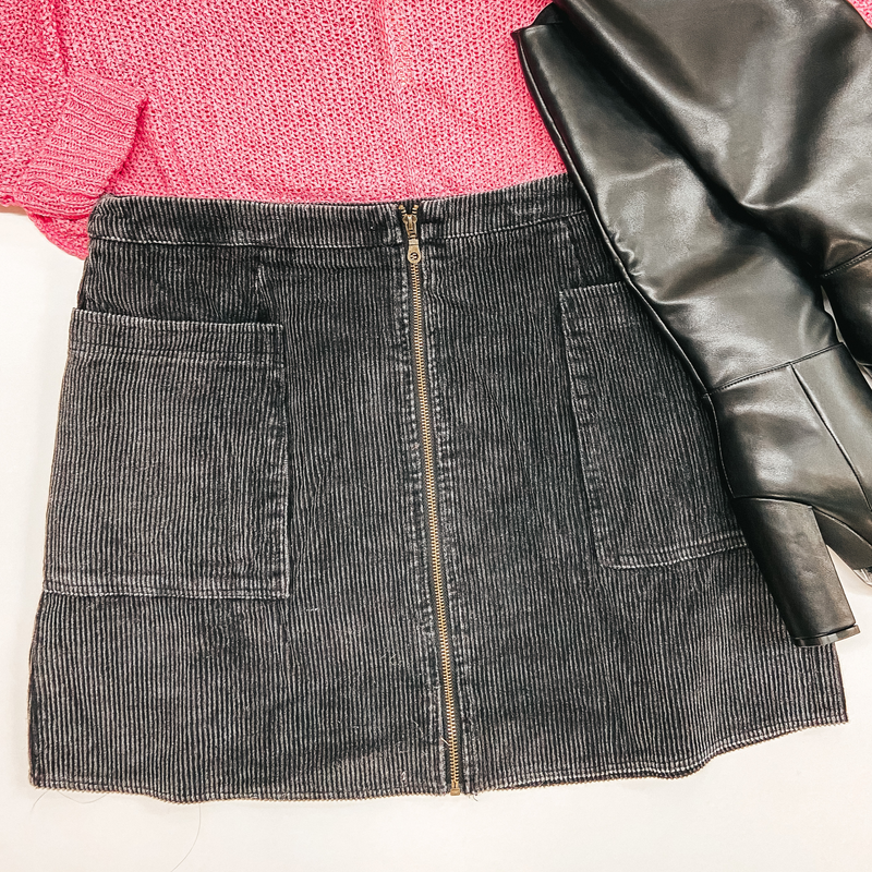 Black corduroy skirt with zipper front and pockets on the hip. Pictured with pink sweater and black booties.