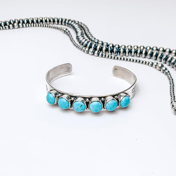 Centered in the picture is a cuff with six kingman turquoise stones. Navajo pearls are laid above the cuff, all on a white background.