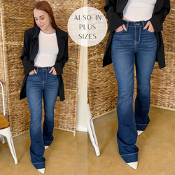 Model is wearing trouser jeans in dark wash. Model has it paired with a white seamless tank top, white booties, and gold jewelry. 